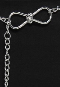 Zilveren metalen ketting met een decoratieve oneindige lus-sluiting, geplaatst tegen een zwarte textiele achtergrond. De bevestigingsmaterialen hebben gladde en glanzende oppervlakken.