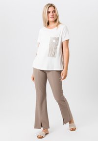 Witte t-shirt met korte mouwen en een vierkant patroon op de zak met franjes, gecombineerd met beige flared broek met ontblote zomen.