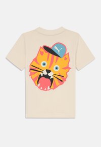 Camiseta de algodón color crema con un gráfico colorido de la cabeza de un tigre que lleva una gorra azul, con acentos en naranja y rosa, grandes ojos redondos y dientes afilados.