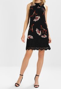 Musta hihaton mekko kukkakuviolla; pitsireunatiedot; istuva muoto; kevyt kangas. Koristeltu punaisilla ja valkoisilla kukilla.