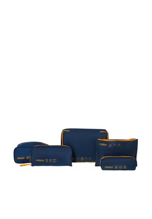 Five navy blue travel organizer bags with orange zippers, labeled with yellow icons indicating specific uses for packing and storage.
