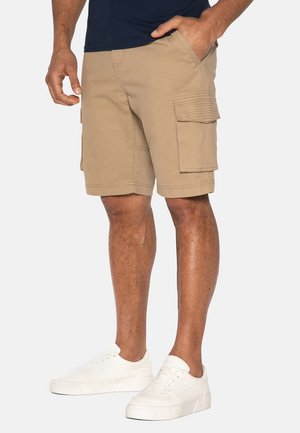 Shorts cargo en khaki en tissu mélangé coton, dotés de deux poches latérales et de deux poches cargo avec fermetures à rabat. Des baskets blanches complètent le look.