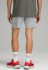 Lysegrå sportsshorts med en blød tekstur, parret med røde sneakers med en pletfri hvid sål, båret med hvide og grå stribede sokker.