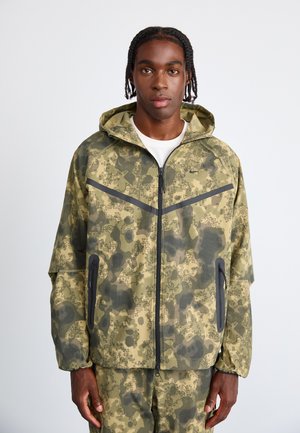 Camouflagemønsteret jakke i nuancer af olivengrøn og sort, med lynlåslukning, hætte og sidelommer med kontrastkant.