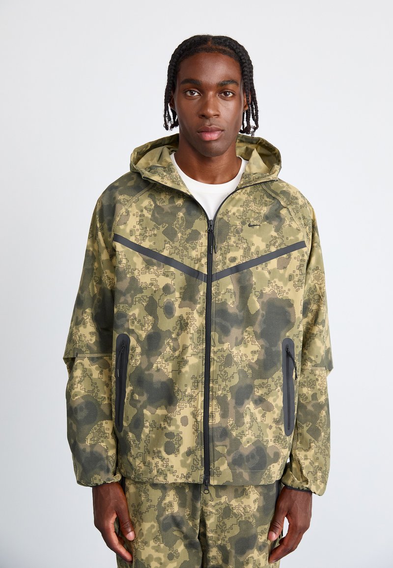 Camouflagemønsteret jakke i nuancer af olivengrøn og sort, med lynlåslukning, hætte og sidelommer med kontrastkant.
