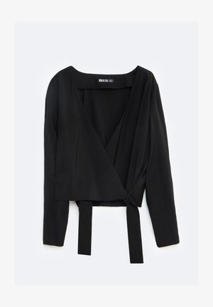 Melnā apvalka blūze, kas izgatavota no gludas auduma, ar garām piedurknēm, dziļu V veida kakla izgriezumu un jostu jostasvietā, lai aizvērtu.