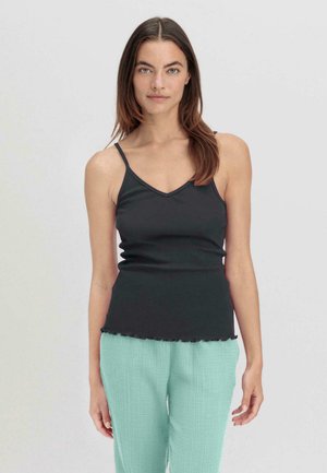 Top nero senza maniche con spalline sottili, scollatura a V e orlo scallop; abbinato a pantaloni verdi menta textured. Tessuto morbido e design aderente.