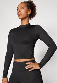 Fekete, hosszú ujjú crop top, sima, rugalmas anyagból készült, oldalon diszkrét logóval és magas nyakkivágással.