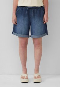 Shorts en denim avec une taille élastique et un cordon de serrage, avec un ourlet roulé, en denim bleu foncé, associés à des sandales à plateforme de couleur claire.
