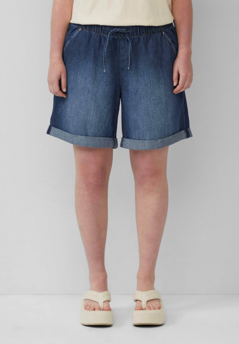 Shorts en denim avec une taille élastique et un cordon de serrage, avec un ourlet roulé, en denim bleu foncé, associés à des sandales à plateforme de couleur claire.