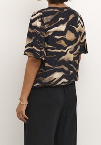Blouse à manches courtes avec un design fluide aux motifs ondulés bleu marine foncé et beige, doté d'une coupe décontractée et d'un tissu doux et léger.