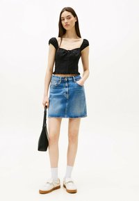 Top nero corto con maniche puff, orlo arricciato, abbinato a una gonna di jeans blu chiaro. Gli accessori includono una piccola borsa nera e sneakers.