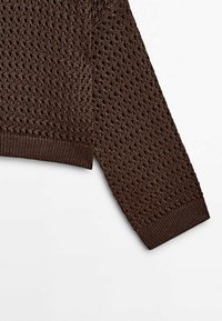 Manche de pull en tricot marron avec un motif en treillis ouvert et un poignet côtelé sur fond blanc.