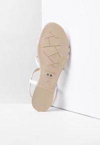 Sandalo bianco con cinturini sottili e suola beige testurizzata. Presenta il logo del marchio e l'impronta di taglia 37, evidenziando un design open-toe.