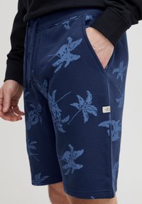 Mornarsko modre kratke hlače s potiskom palminega lista v svetlo modri barvi, z elastičnim pasom in stranskimi žepi. Mehka tkanina.