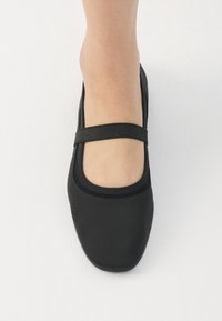 Ballerine nere con punta arrotondata, fascetta elastica sul dorso del piede, tessuto liscio e suola texturizzata. Design semplice e minimalista.
