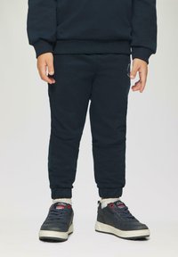 Navy sweatshirt en bijpassende joggers met elastische cuffs, gecombineerd met donkere sneakers met rode accenten en witte zolen.