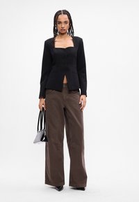 Melns žakets ar kvadrātu formu apakšējo daļu, piecām priekšējām pogām un divām sānu kabatām; apvienots ar pārāk lielām brūnām biksēm un mazu melnu somu.