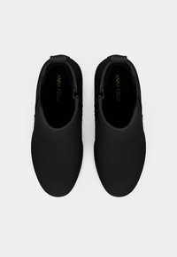 Czarne buty wsuwane o gładkiej, matowej fakturze, zaokrąglonym czubku i elastycznych panelach bocznych. Wnętrze ozdobione jest złotym napisem marki.