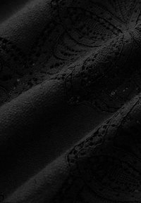Tissu noir avec des motifs de dentelle complexes et des textures, montrant des plis et une broderie délicate et détaillée.