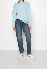 Sudadera de color azul claro con diseño impreso, jeans de pierna recta de color azul oscuro y zapatillas blancas con acentos en navy. Atuendo casual con un corte relajado.