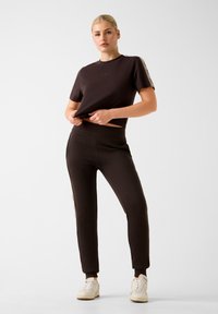 Czarny krótki t-shirt z krótkimi rękawami, w zestawieniu z dopasowanymi czarnymi dresami z bocznymi paskami i elastycznym pasem; model stoi pewnie.