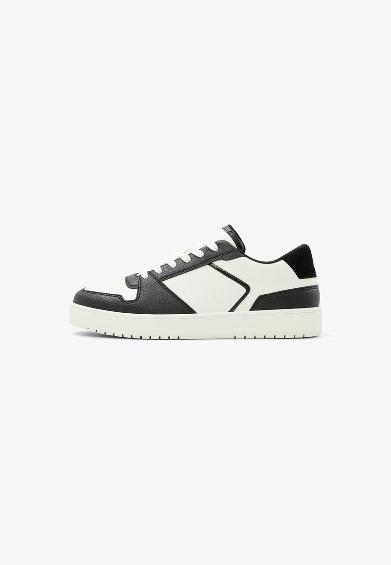 White and black sneaker featuring a smooth leather finish, textured accents, round toe, and a cushioned sole with patterned tread.