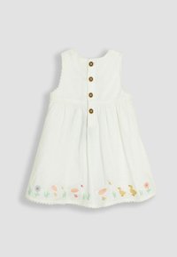 Witte mouwloze jurk met een ronde halslijn, vijf bruine knopen aan de achterkant en geborduurde eenden en bloemen aan de zoom.