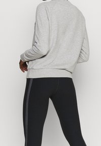 Sweat-shirt en polaire grise à coupe décontractée avec ourlet côtelé, associé à des leggings noirs ajustés avec une bande latérale contrastante.