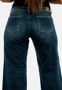 Jeans in denim blu scuro con vita alta, gamba larga, cuciture distintive sui taschini posteriori e una piccola etichetta in pelle in vita.