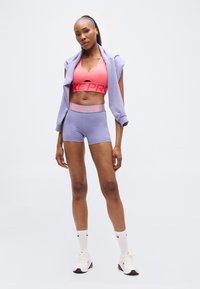 Αθλητική εμφάνιση Nike Pro που περιλαμβάνει ροζ αθλητικό σουτιέν, λιλά σορτς με λογότυπο στη μέση και αντίστοιχο ανοιχτό λιλά μπουφάν με φερμουάρ.