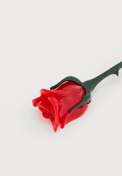 Rose en verre rouge avec une tige vert foncé sur un fond blanc uni, présentant des surfaces lisses et brillantes ainsi que des formes délicates de pétales.