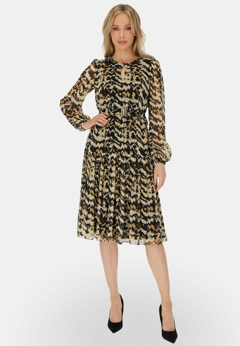 Sukienka w odcieniach czerni, beżu i brązu. Posiada długie rękawy, okrągły dekolt z detalem w kształcie dziurki oraz zwiewną spódnicę.