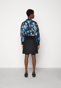 Suéter corto con un patrón floral en tonos marinos y acentos vibrantes en rosa y azul, combinado con una falda negra hasta la rodilla y zapatos negros.