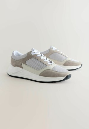 Grey and white sneakers feature mesh and suede materials, a rounded toe, flat laces, and a textured rubber sole with a slight heel.