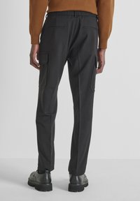 Zwarte, stijlvolle broek met een ontspannen pasvorm, voorzien van zijvakjes en een elastische tailleband. Het materiaal lijkt glad en duurzaam te zijn.