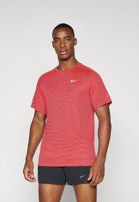 Piros Nike sportpóló texturált anyagból készült, rövid ujjal és kerek nyakkivágással, a mellkason egy kis fehér logóval.