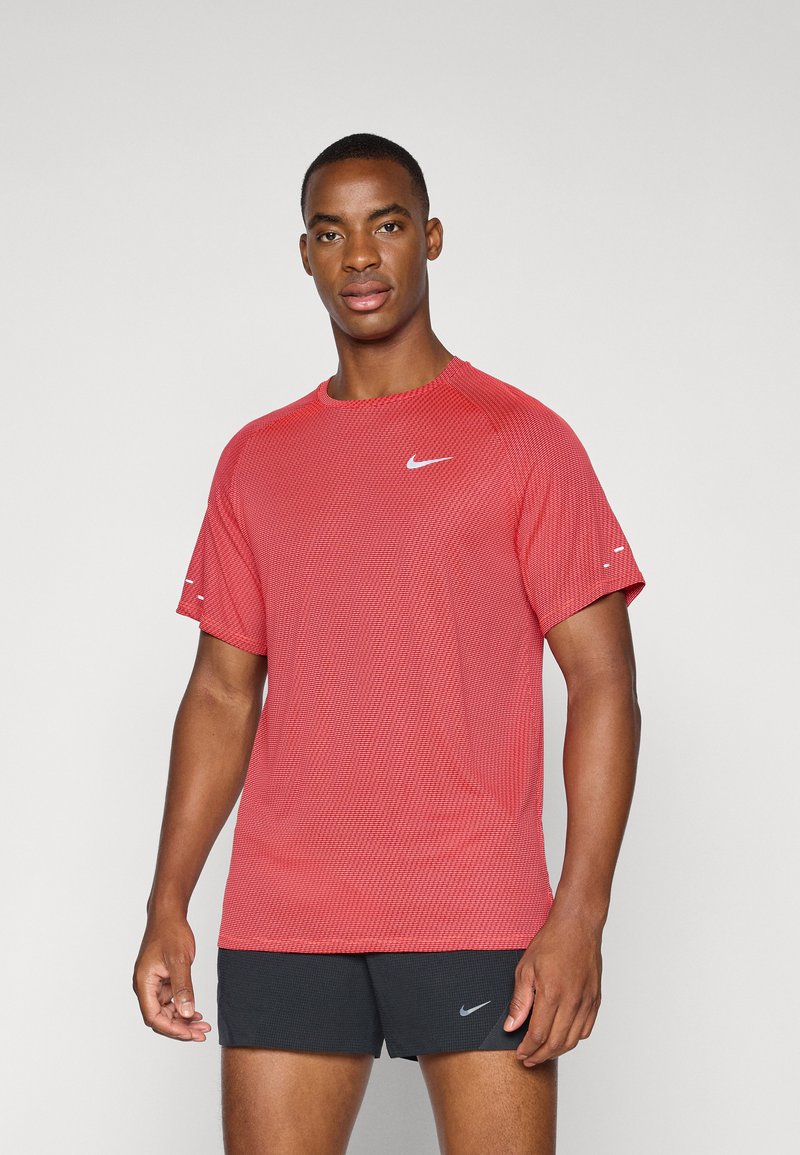 Piros Nike sportpóló texturált anyagból készült, rövid ujjal és kerek nyakkivágással, a mellkason egy kis fehér logóval.