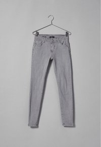 Vaqueros skinnys de denim gris con un diseño clásico de cinco bolsillos, lazos para cinturón y detalles de costura sutiles. La tela parece ligeramente texturizada.