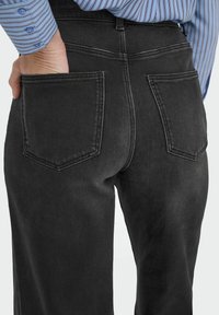 Jean en denim gris foncé avec un design ajusté, deux poches arrière avec des bords cousus et une texture lisse.
