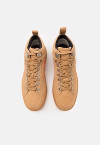 Bruna mockaskor med hög häl och orange detaljer, silvriga ögla och kontrasterande svart foder. Tjock gummisula.