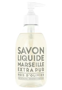 Clear glass bottle with a white pump dispenser, filled with liquid soap. Label features gray text: "Savon Liquide Marseille Extra Pur Bois d'Olivier."
