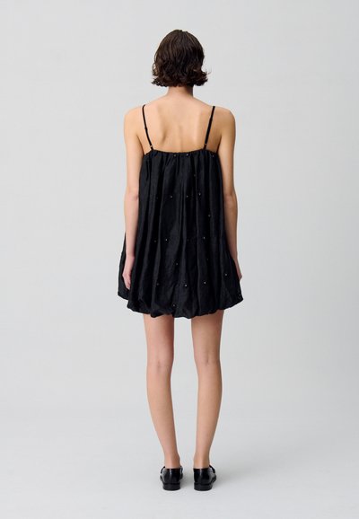 Vestido negro sin mangas con un corte holgado, que presenta una parte trasera fruncida y adornado con pequeñas tachuelas decorativas. Tela suave y ligera.