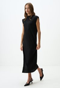 Schwarzes, plissiertes Midi-Kleid mit kurzen Ärmeln und hohem Kragen. Verfügt über eine glatte Textur und eine lockere Passform, kombiniert mit schwarzen, hohen Mules.
