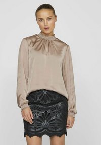 Silkeblond bluse med flæsekrave og lange ærmer, parret med en sort, detaljeret mønstret blonde med bølget kant.