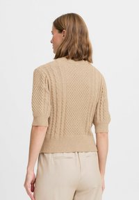 Maglione beige a maglia con maniche corte, orlo a costine e motivo testurizzato. La vista posteriore rivela una silhouette aderente.