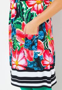 Sukienka w kwiaty z dużymi różowymi i czerwonymi kwiatami na czarnym tle, z przednią kieszonką i poziomymi białymi oraz czarnymi paskami na brzegu.