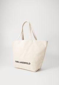 Šviesiai ruda drobinė pirkinių maišelis su dviem petnešomis ir juodu „KARL LAGERFELD“ logotipu apačioje. Lygus paviršius ir erdvus dizainas.