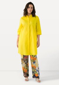 Camicia gialla con maniche a tre quarti abbinata a pantaloni con motivo di arance e colori vivaci. Tessuto di cotone testurizzato.