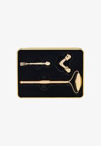 Set di strumenti per la cura della pelle in tonalità oro, presentato in una scatola foderata in velluto nero, contenente un rullo di giada, un massaggiatore a due teste e un piccolo cucchiaio.